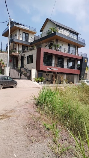 A multi-story building with a modern architectural design, featuring balconies with railings and potted plants.