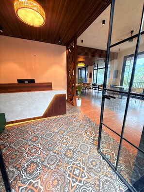 Un hall d’hôtel avec un sol à motifs, un comptoir d’accueil et une vue sur l’extérieur grâce à de grandes fenêtres.