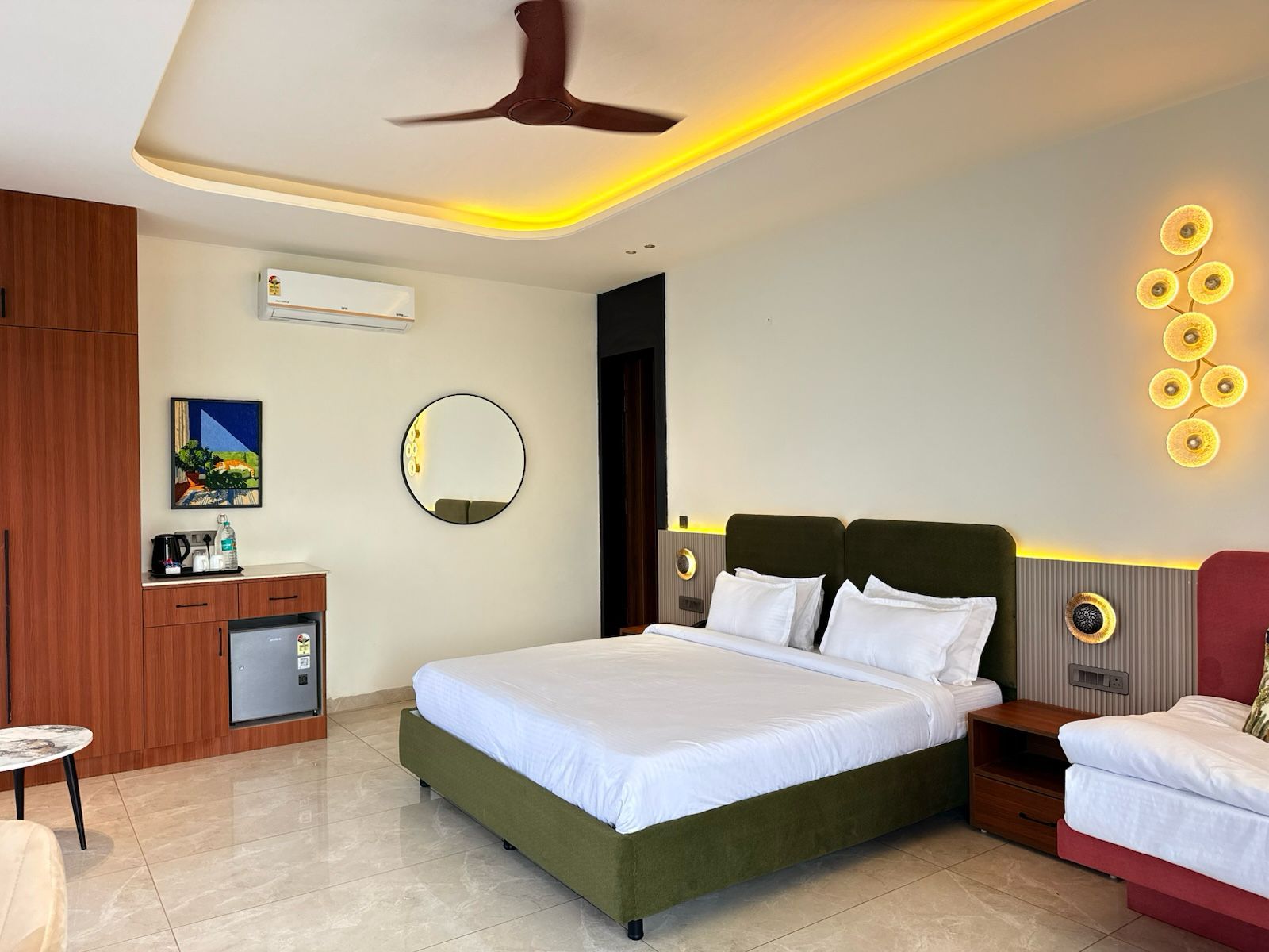 A hotel room with a bed, bedside tables, a desk with a chair, a round mirror, and a ceiling fan.