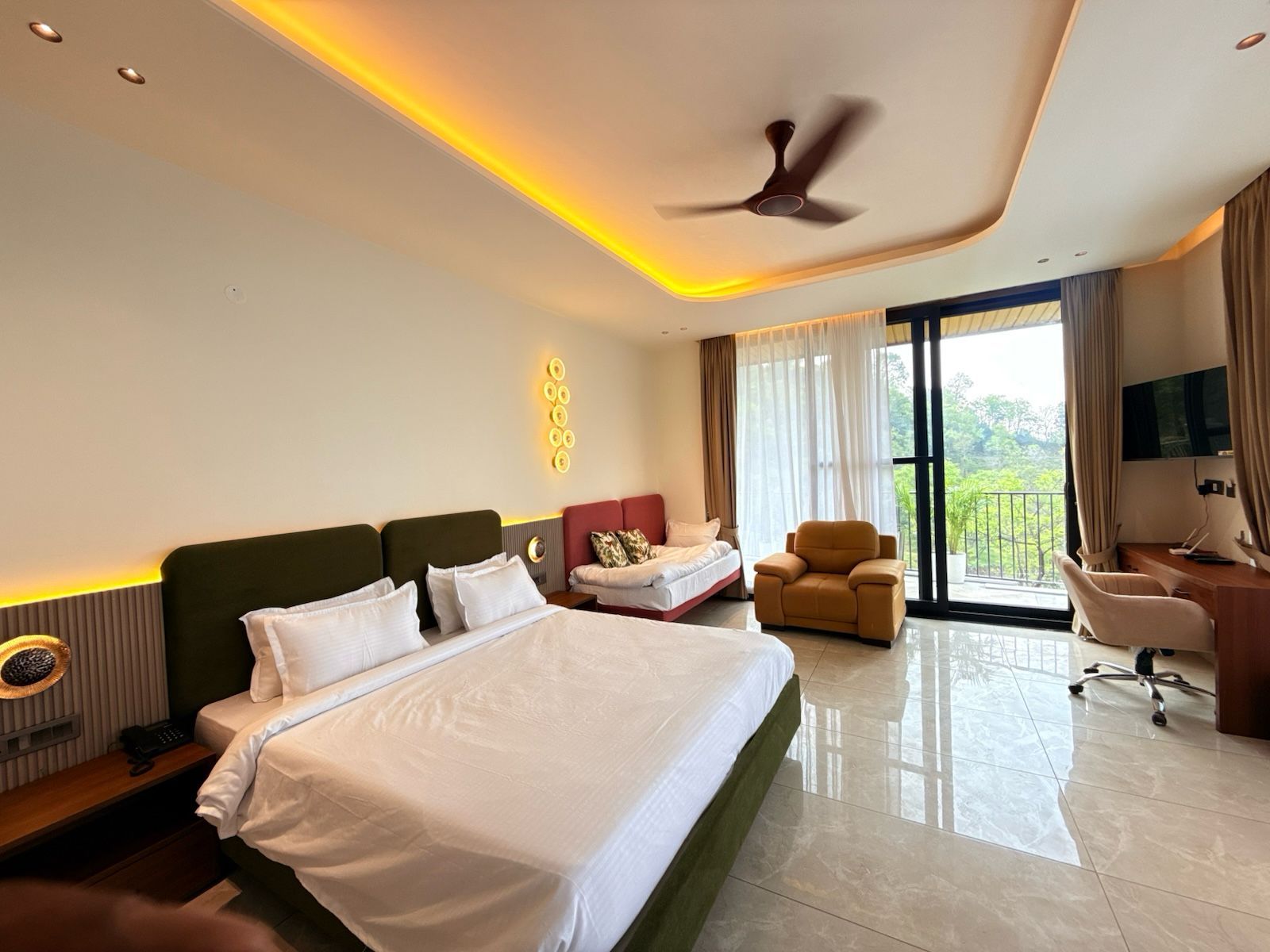 A hotel room with a large bed, a desk, a chair, and a balcony with a view.