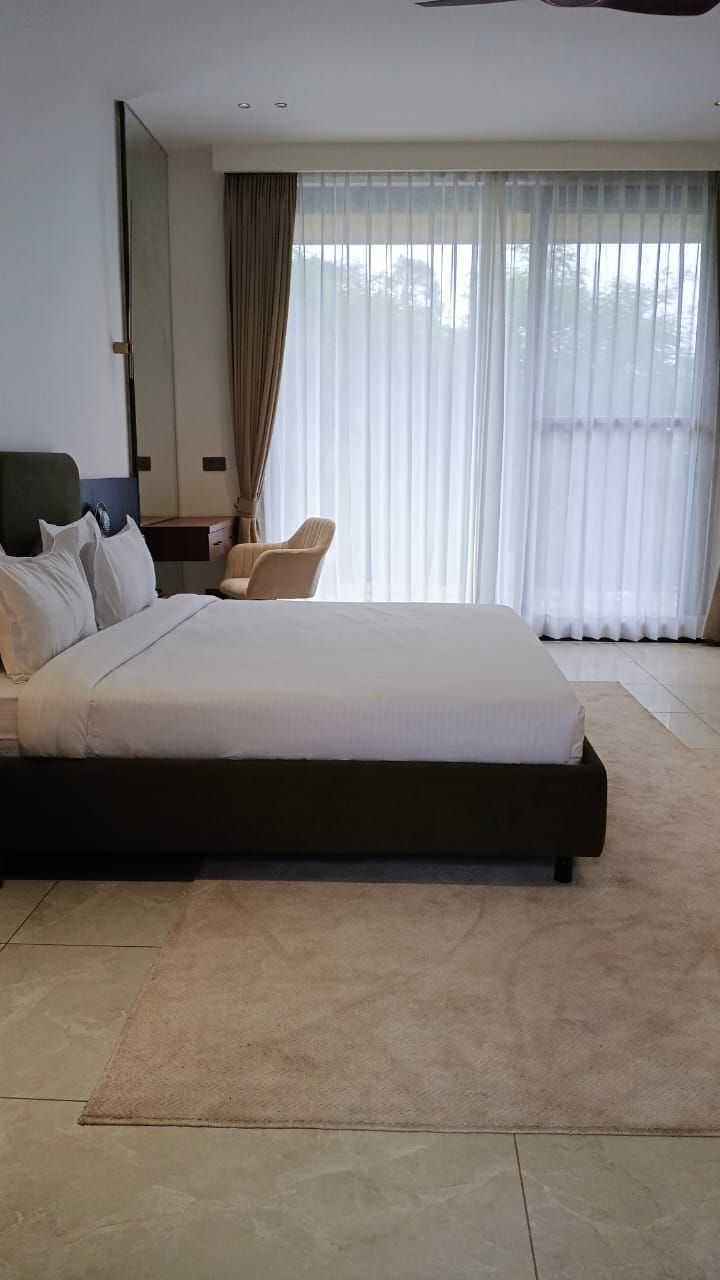 Une chambre d’hôtel moderne avec un grand lit, une chaise, un bureau et une grande fenêtre avec des rideaux.