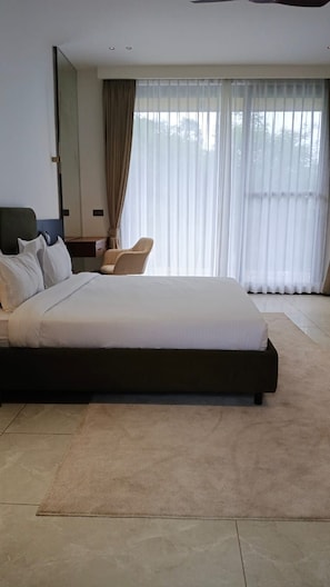 A modern hotel room with a large bed, a chair, a desk, and a large window with curtains.