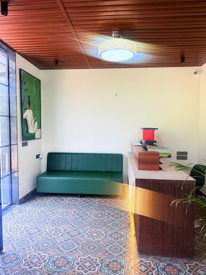 Una habitación con un sofá verde, un mostrador de recepción de madera, baldosas de suelo estampadas y un cuadro en la pared.