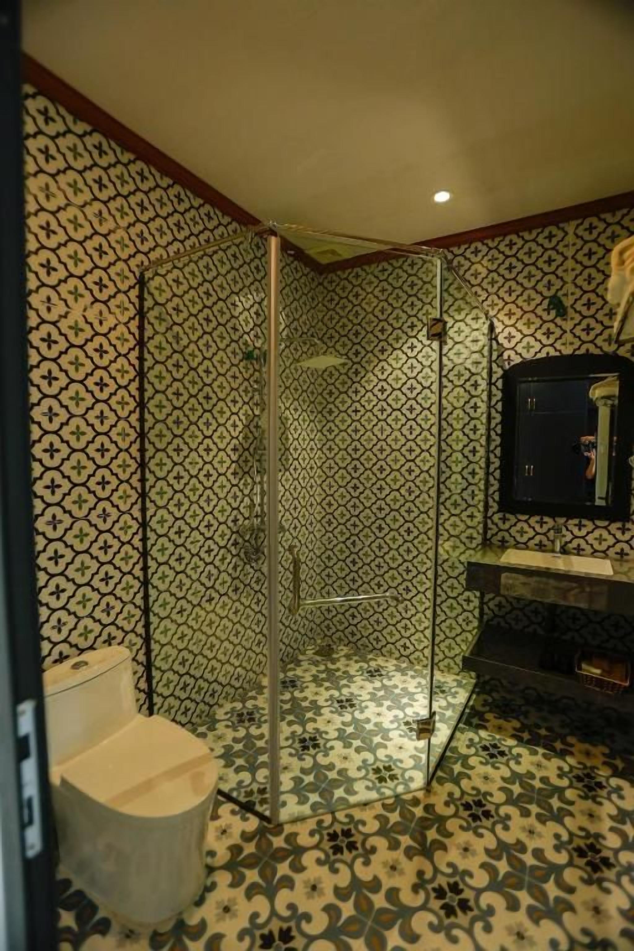Un baño con piso de baldosas estampadas, cabina de ducha de vidrio y un inodoro.