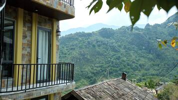 A multi-story building with a balcony, stone facade, and a view of a forested mountain range.