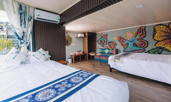 Habitación de hotel con dos camas, un mural de una mariposa colorida y vista al exterior.
