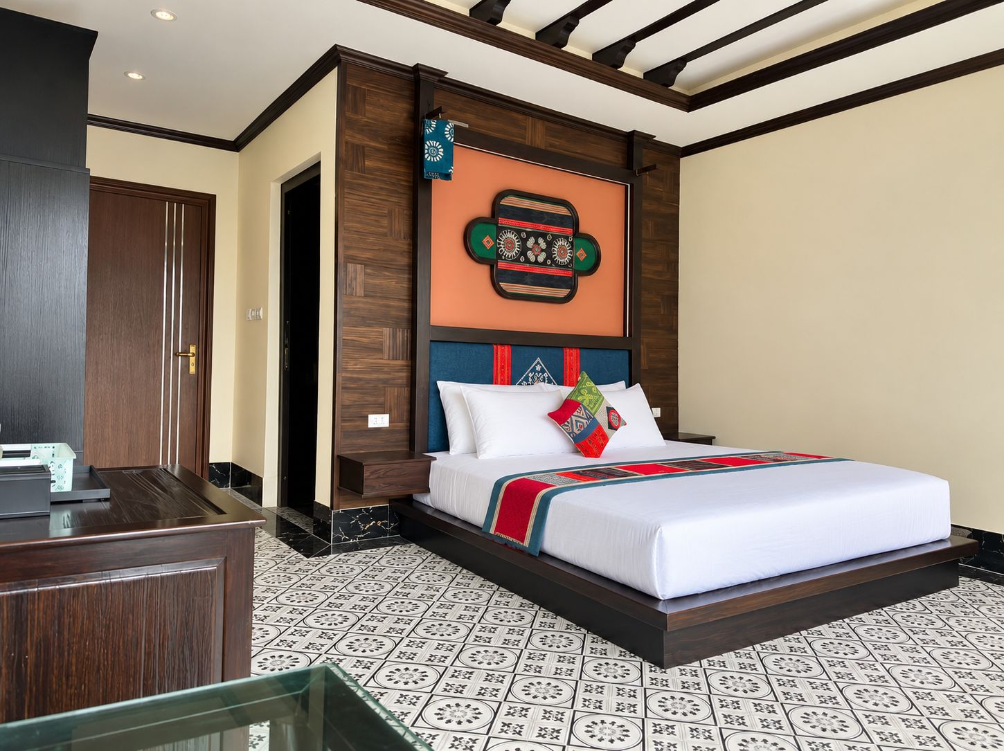 Una habitación de hotel con una cama, cabecero de madera, pared con un tapiz decorativo y suelo estampado.