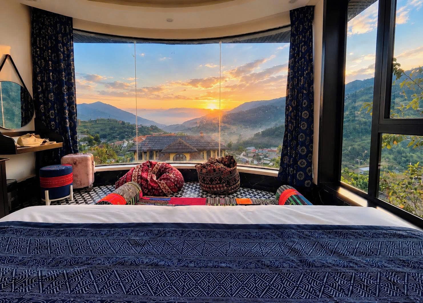 A room with a large bed, a view of mountains, and a sunset.