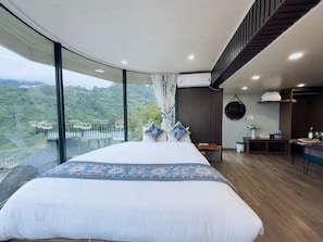 A modern bedroom with a large bed, a view of a lush landscape, and a dining area with a table and chairs. - Lan Rung Retreat Sapa (Sa Pa)