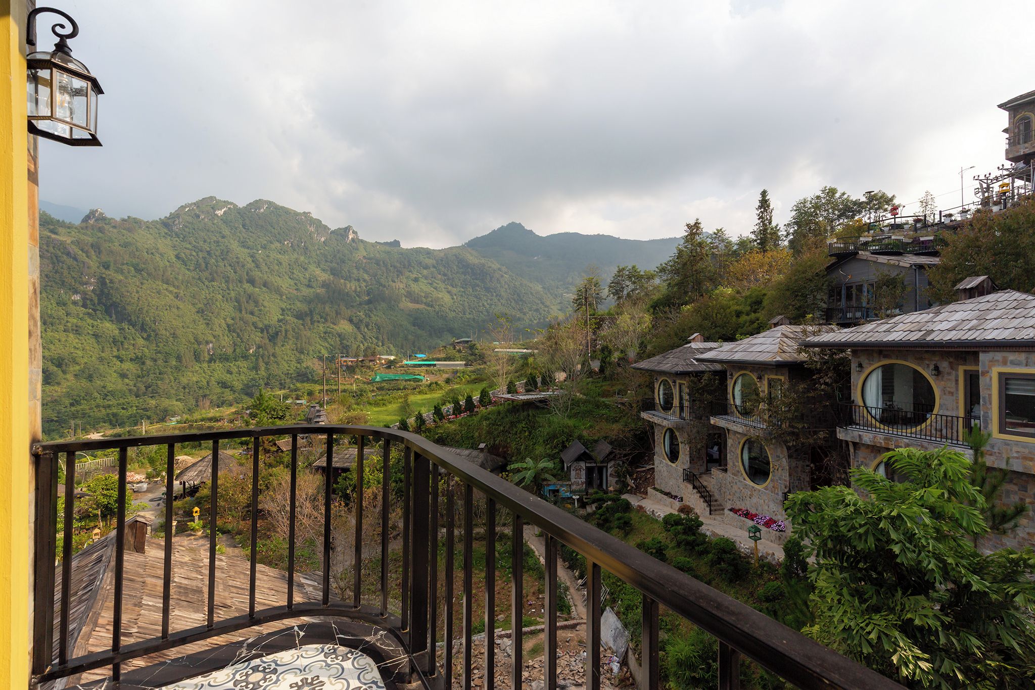 Un balcón con vistas a un paisaje montañoso, un edificio de piedra con ventanas circulares y una pared amarilla.