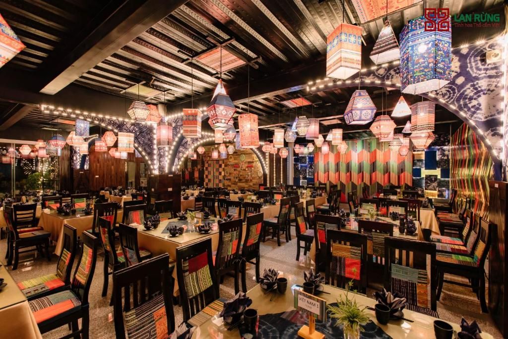 A restaurant with multiple tables and chairs, decorated with hanging lanterns and traditional Vietnamese textiles.