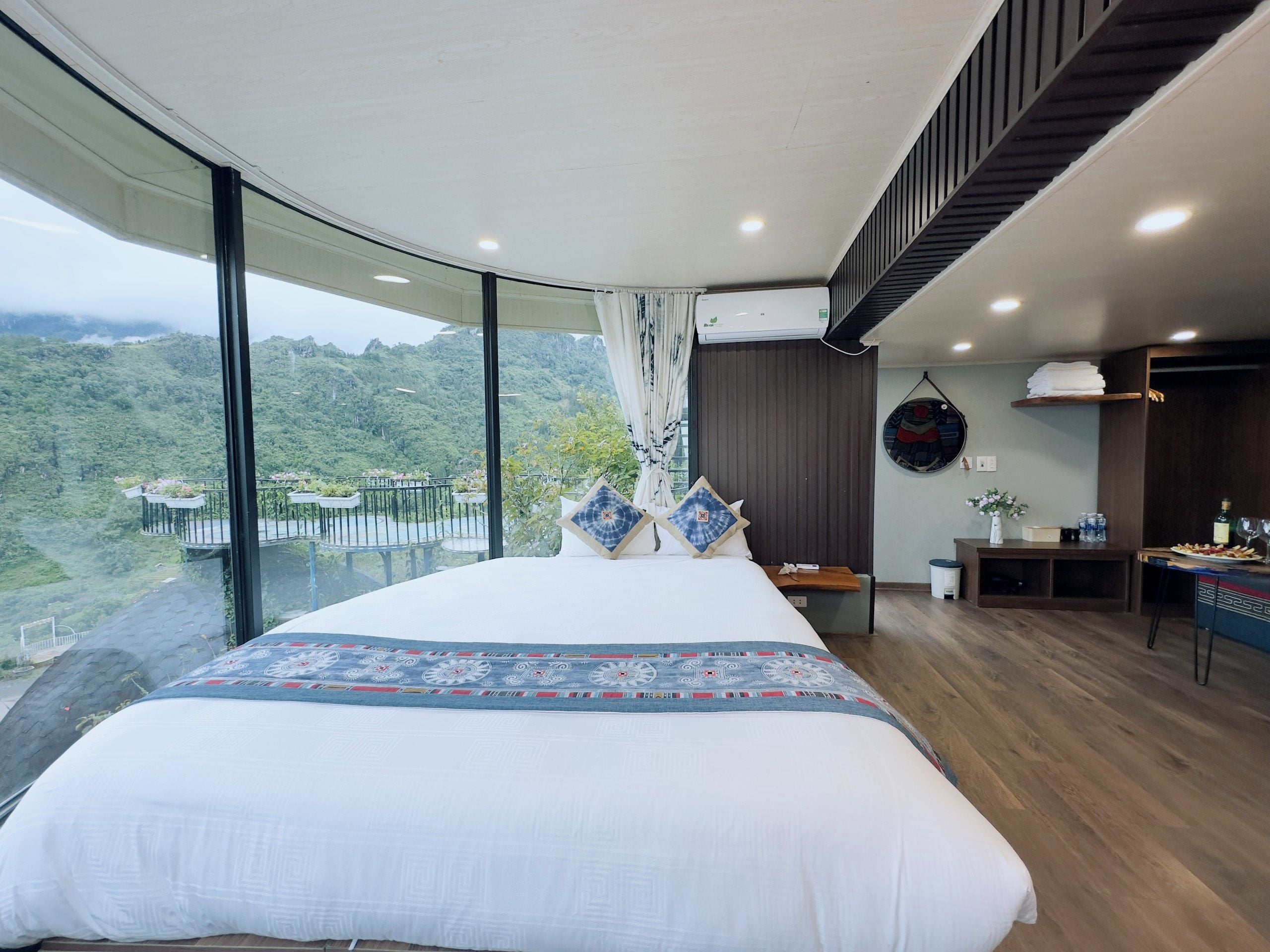 A bedroom with a large bed, a dining area, and a view of a mountainous landscape.