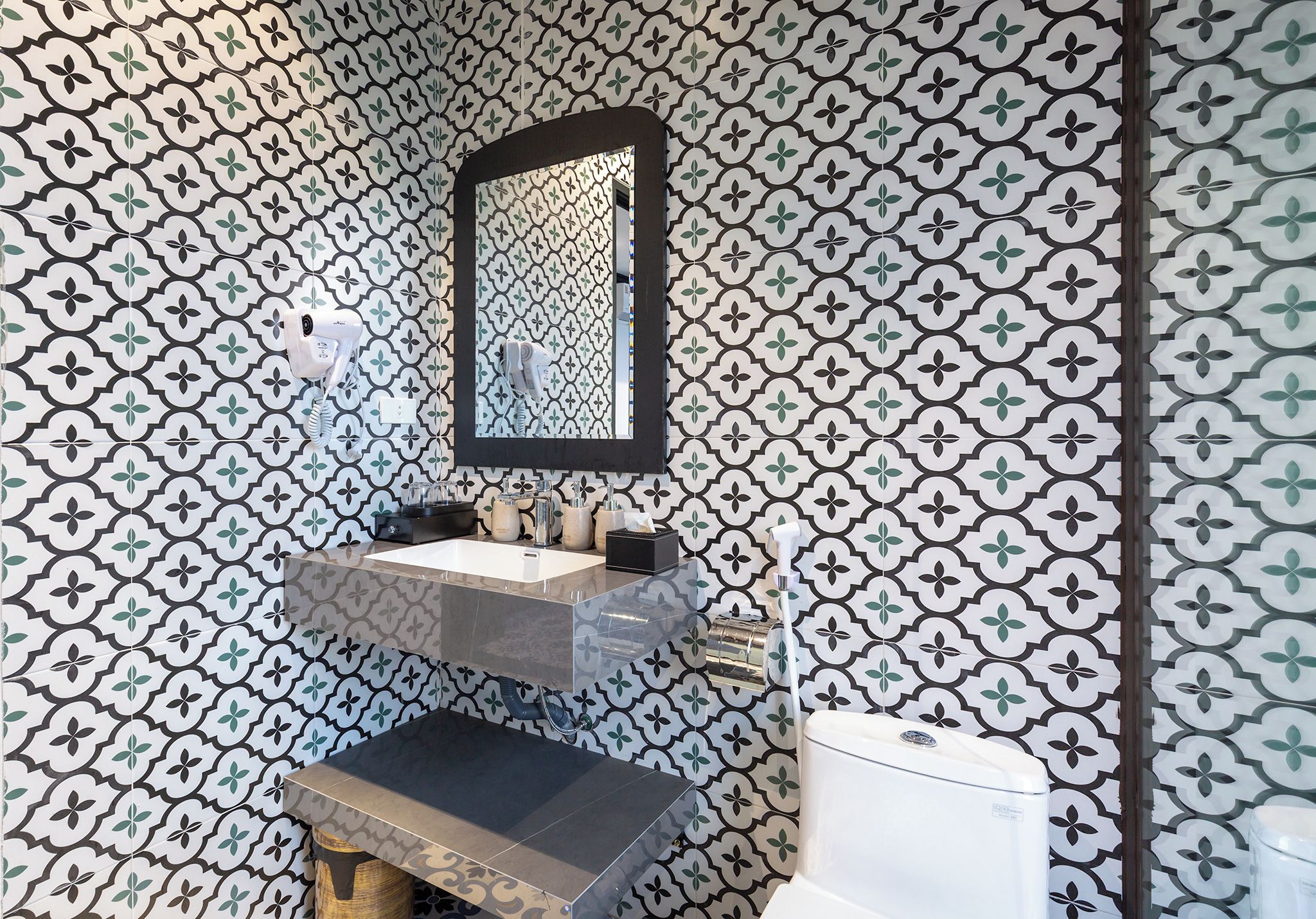 Un baño con pared estampada, un espejo, un lavamanos y un inodoro.