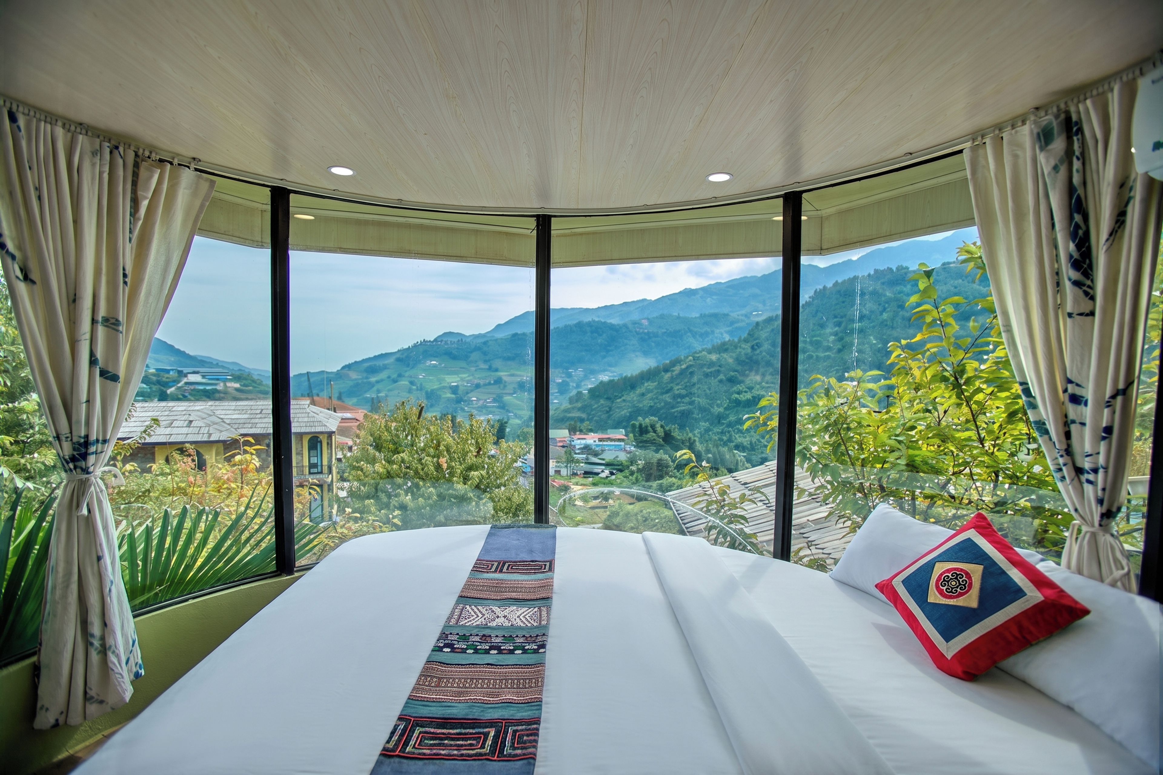 Une chambre avec un grand lit, une vue sur les montagnes et des rideaux.