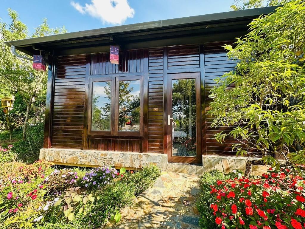 Una cabaña de madera con base de piedra, ventanas amplias y un jardín con diversas flores.