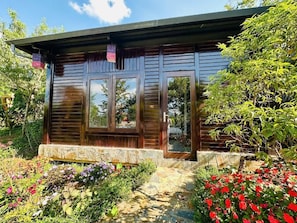 Una cabaña de madera con base de piedra, ventanas amplias y un jardín con diversas flores.