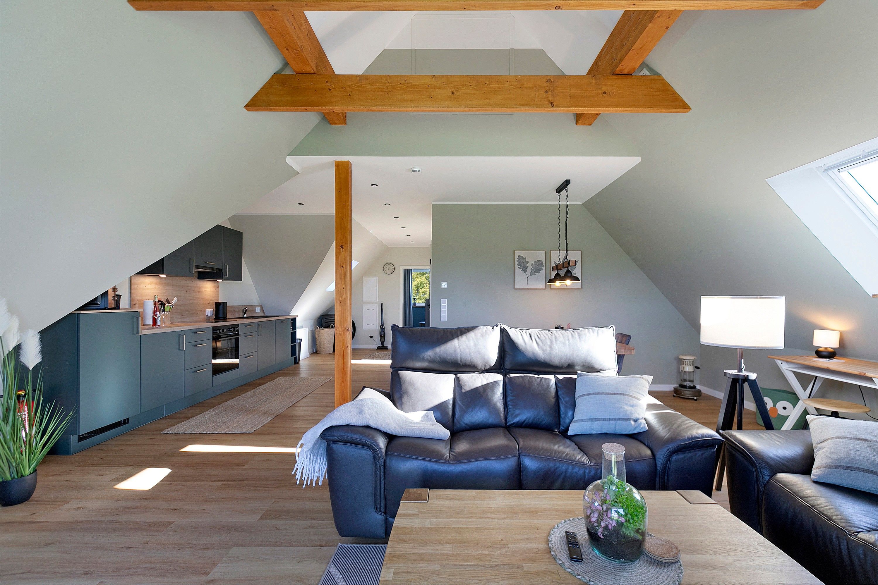 En rummelig loftrum med højt til loftet, et spiseområde, en opholdsstue med lædersofa og et køkken med moderne hårde hvidevarer.