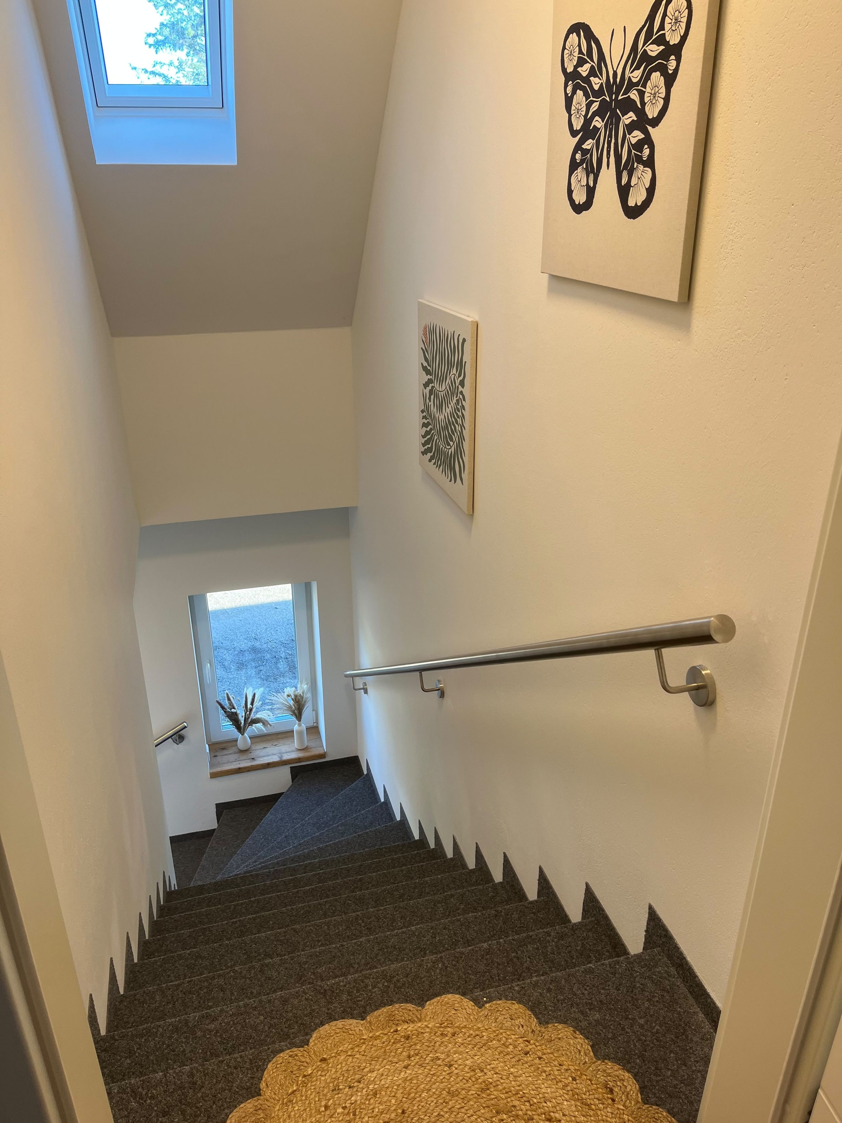 Un escalier avec une rampe, une lucarne et des œuvres d’art accrochées aux murs.
