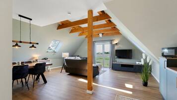 Un loft moderne comprenant un espace repas, une cuisine et un salon, avec des poutres en bois, de grandes fenêtres et un téléviseur à écran plat.