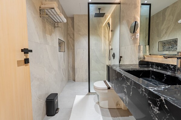 Un baño moderno con ducha envuelta en vidrio, lavamanos de mármol negro y un inodoro.
