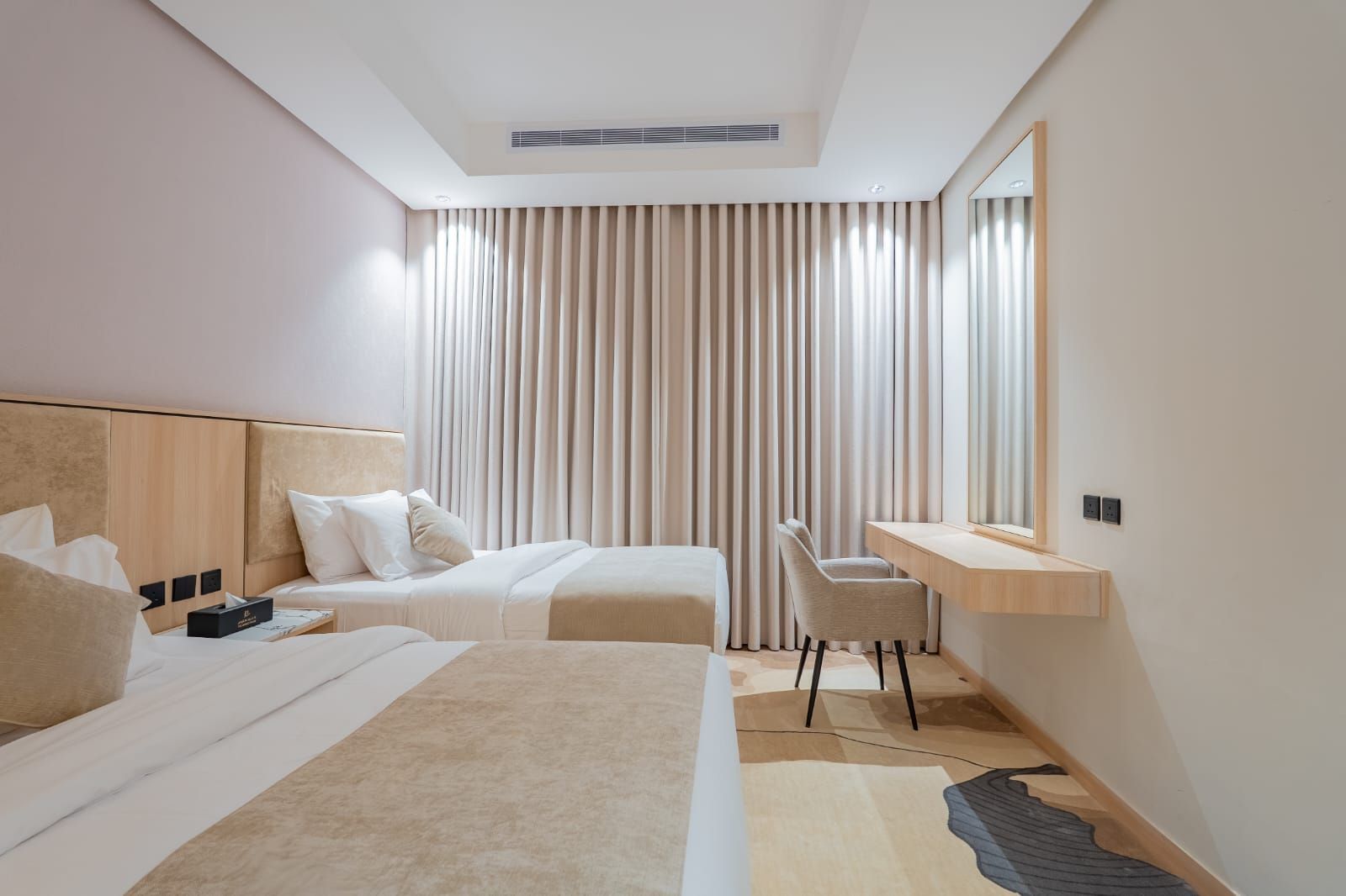 Una habitación de hotel moderna con dos camas, un escritorio y un amplio ventanal con cortinas.