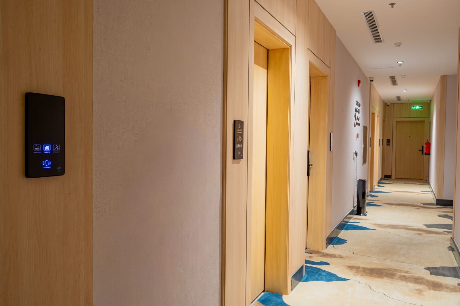 A hotel hallway with a digital keypad, wooden doors, and a carpeted floor.