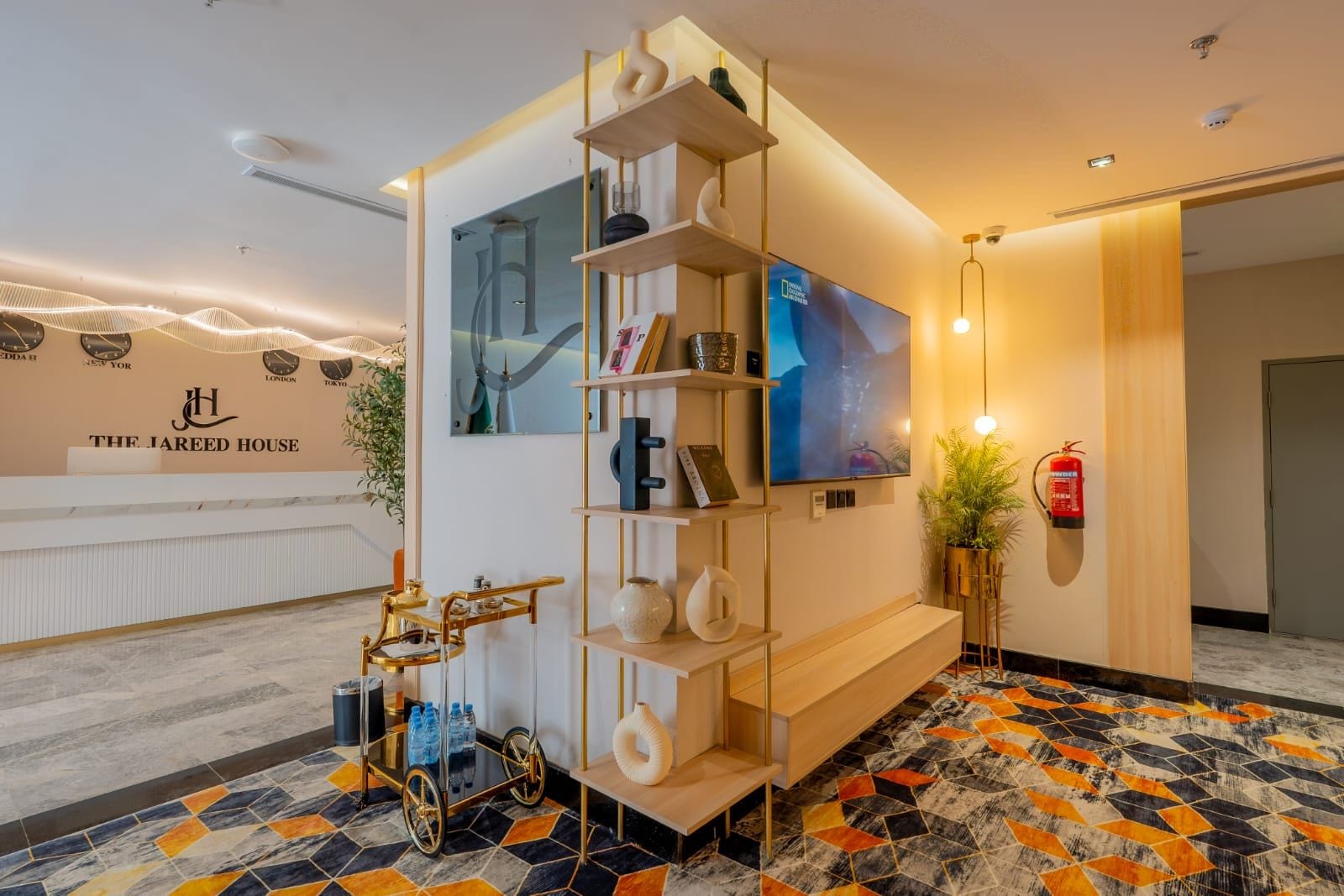 Una zona d'arribada amb un disseny modern, que inclou una recepció, una televisió penjada a la paret i una paret decorativa amb noms de ciutats.
