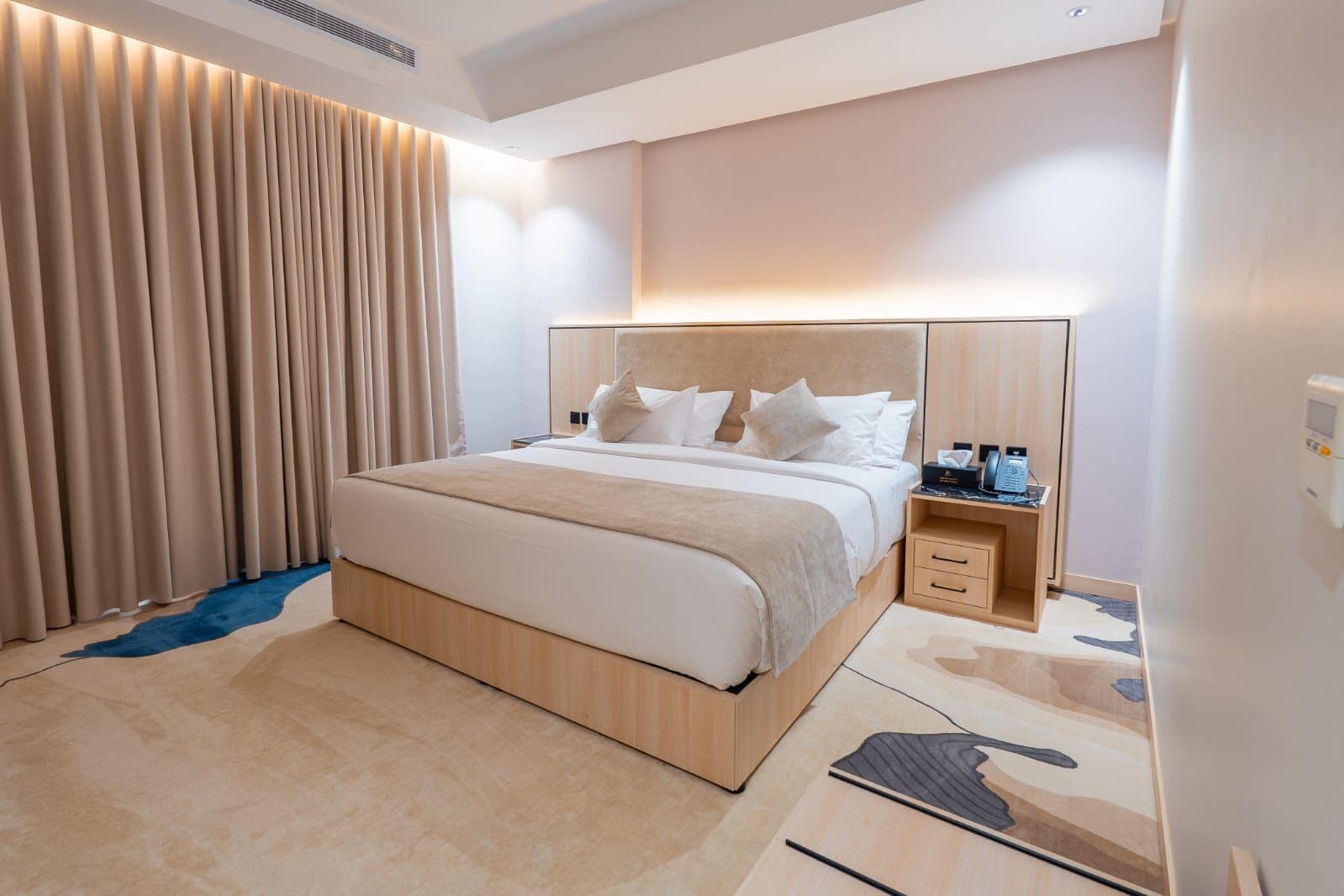 A modern hotel room with a large bed, bedside tables, and a built-in desk.