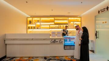 A coffee bar with a marble countertop and a refrigerated display, a sign indicating a toilet, and a patterned floor.