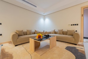 Un salon moderne avec un canapé beige, une table basse et un panier de fruits.