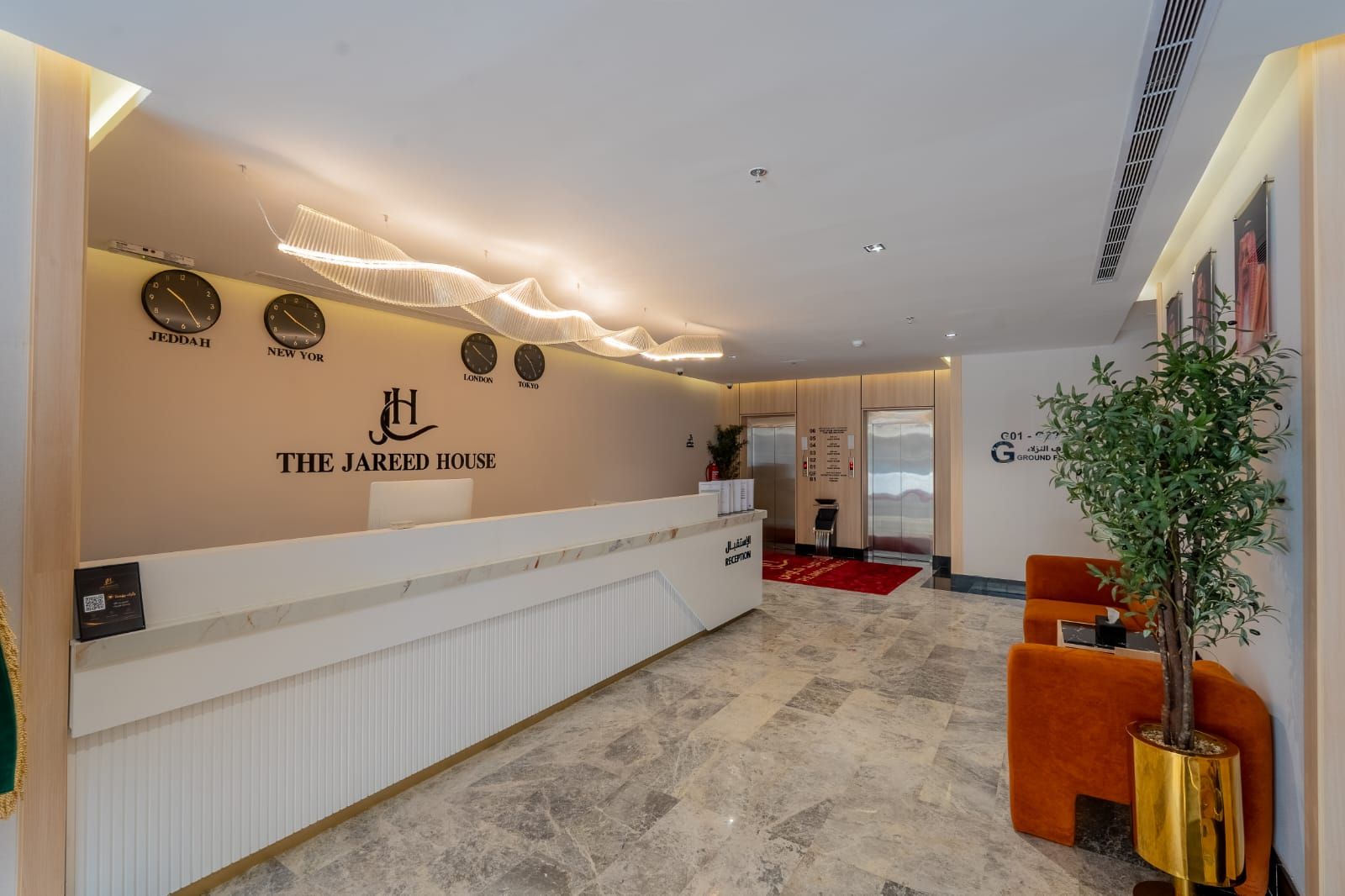 A hotel reception area with a reception desk, clocks displaying different cities, and a red carpet leading to elevators.