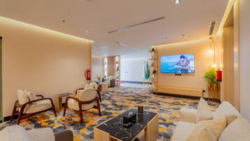 A hotel lobby with seating areas, a television screen, and a patterned floor.
