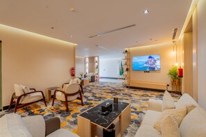 Een hotel lobby met zitgedeeltes, een televisiescherm en een vloer met patroon.