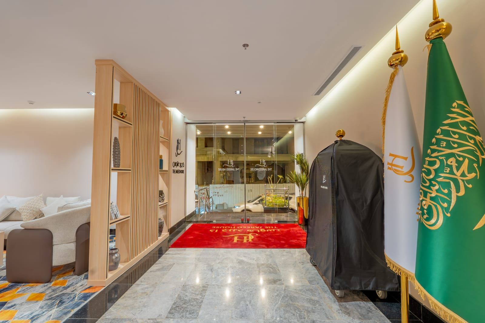 Un vestíbulo de hotel con alfombra roja, un sofá, una estantería de madera y una bandera.