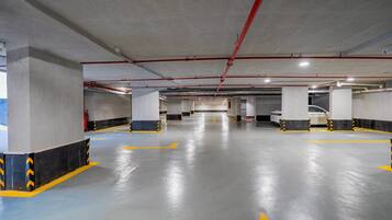 A multi-level parking garage with concrete pillars, yellow directional arrows, and red pipes on the ceiling.
