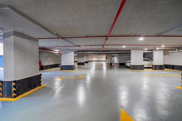 Un estacionamiento de varios niveles con pilares de concreto, flechas amarillas direccionales y tuberías rojas en el techo.