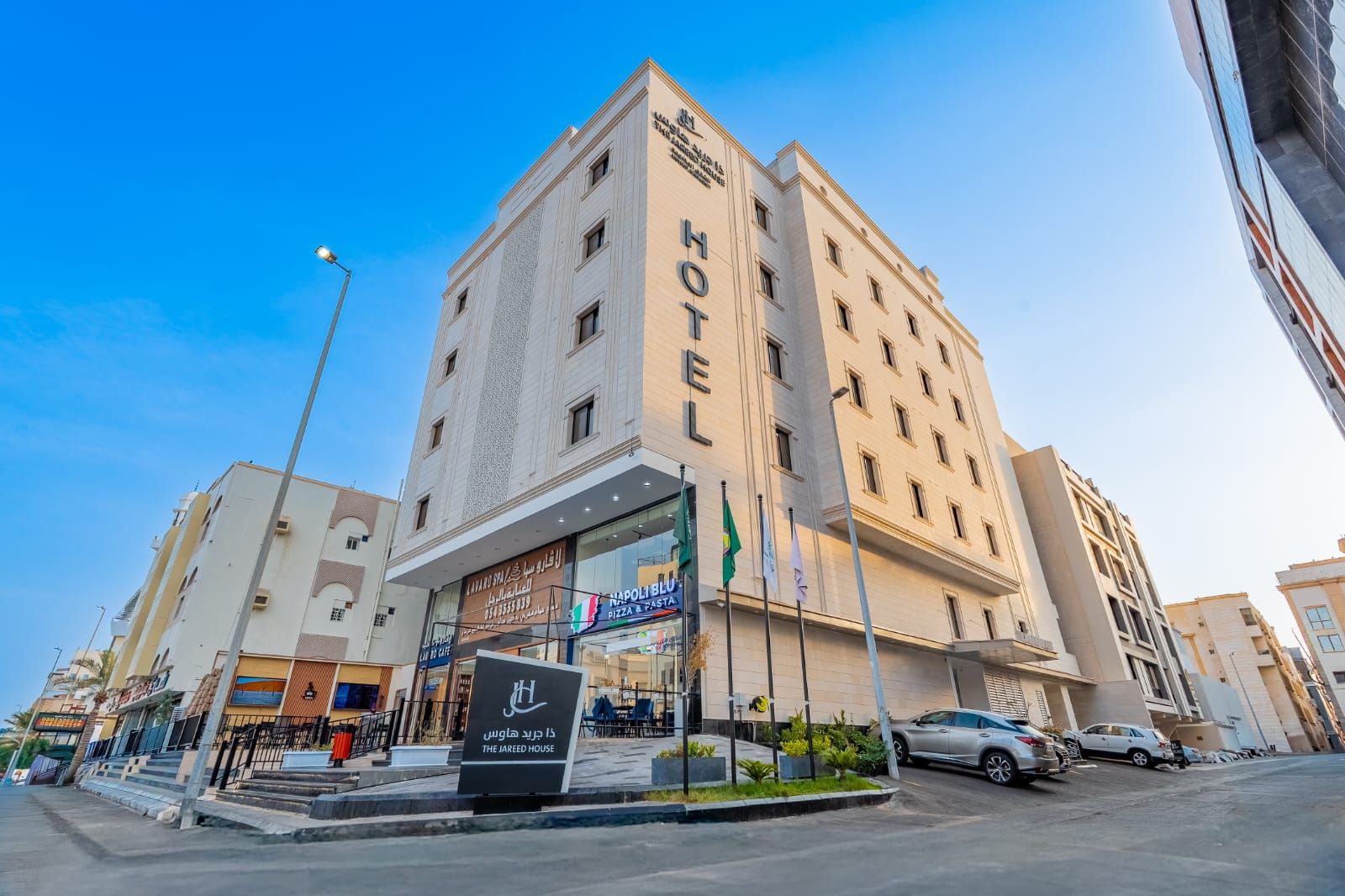 A hotel with a prominent 'HOTEL' sign, a restaurant named 'NAPOLI BLUE' on the ground floor, and a sign for 'THE JAREED HOUSE' in front.