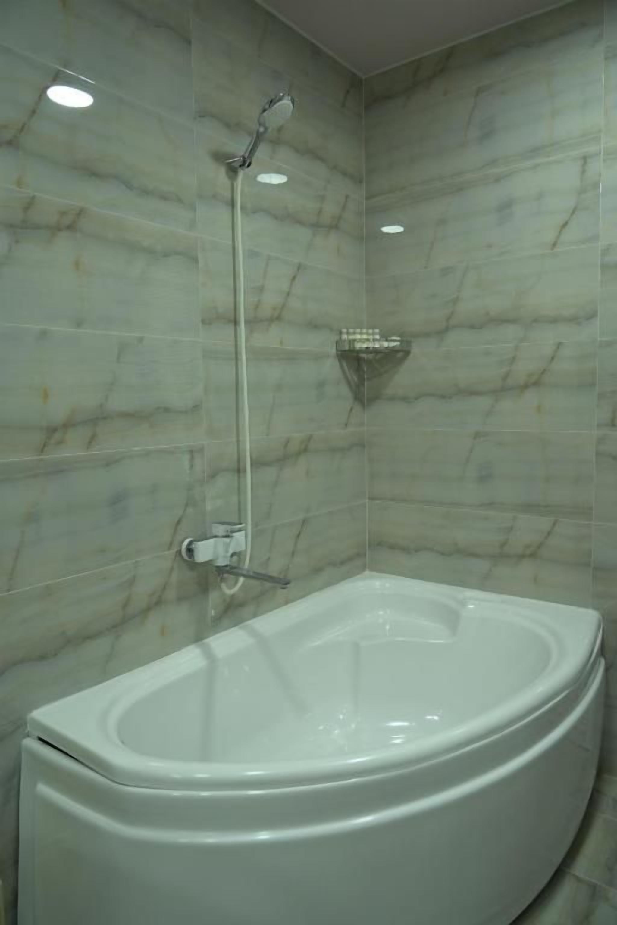 A bathroom with a freestanding bathtub, a showerhead, and a wall-mounted shelf.