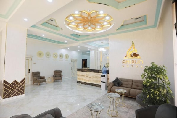 Vestíbulo de hotel con mostrador de recepción, zona de estar y una lámpara decorativa grande en el techo.