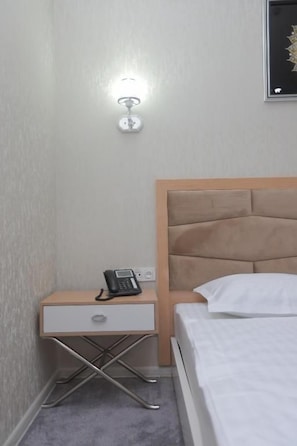 Una habitació d'hotel amb un llit, una taula de nit amb un telèfon i una làmpada de paret.