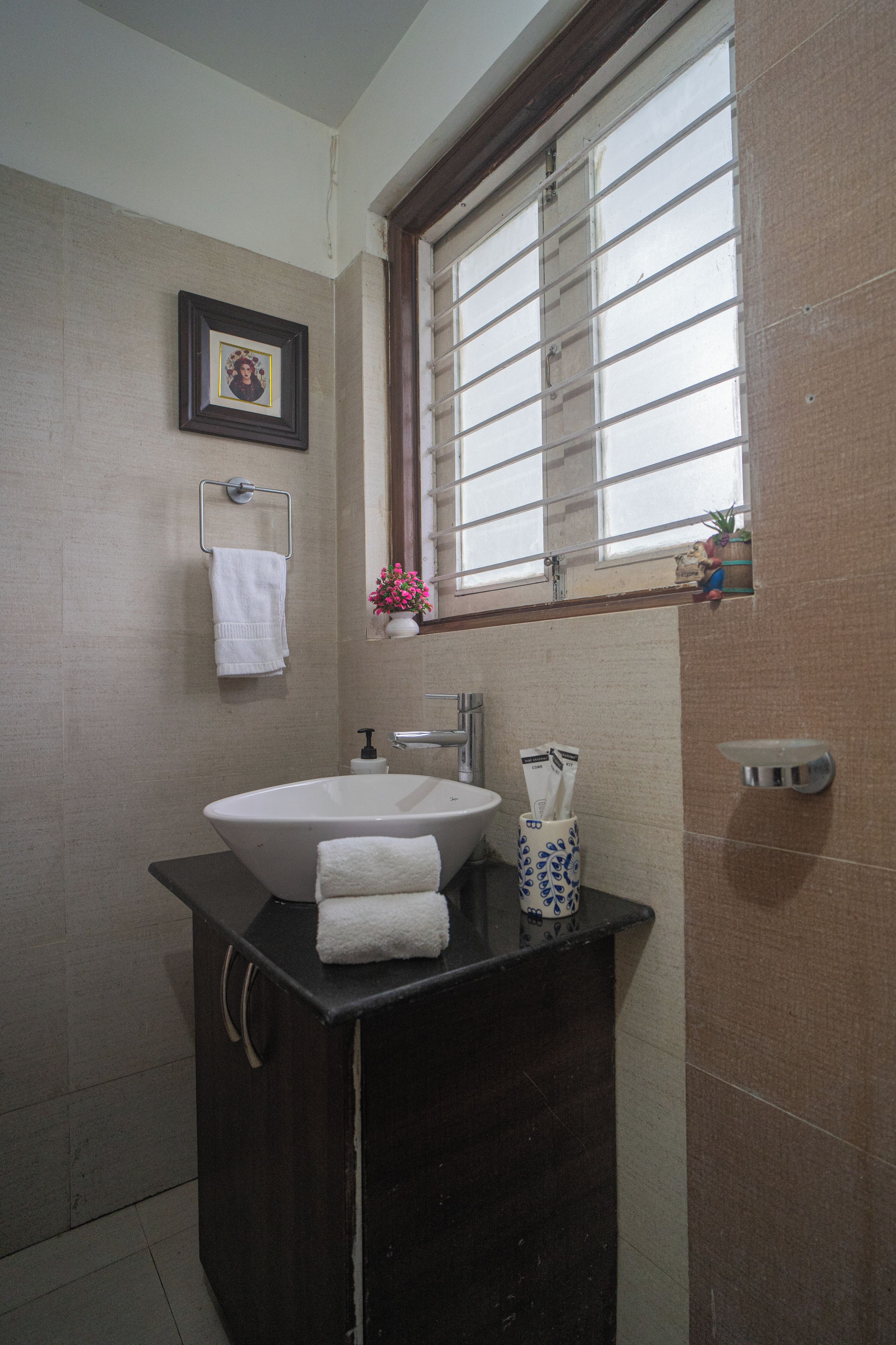 Une salle de bain avec un lavabo blanc, un plan de toilette foncé et une fenêtre avec des stores.