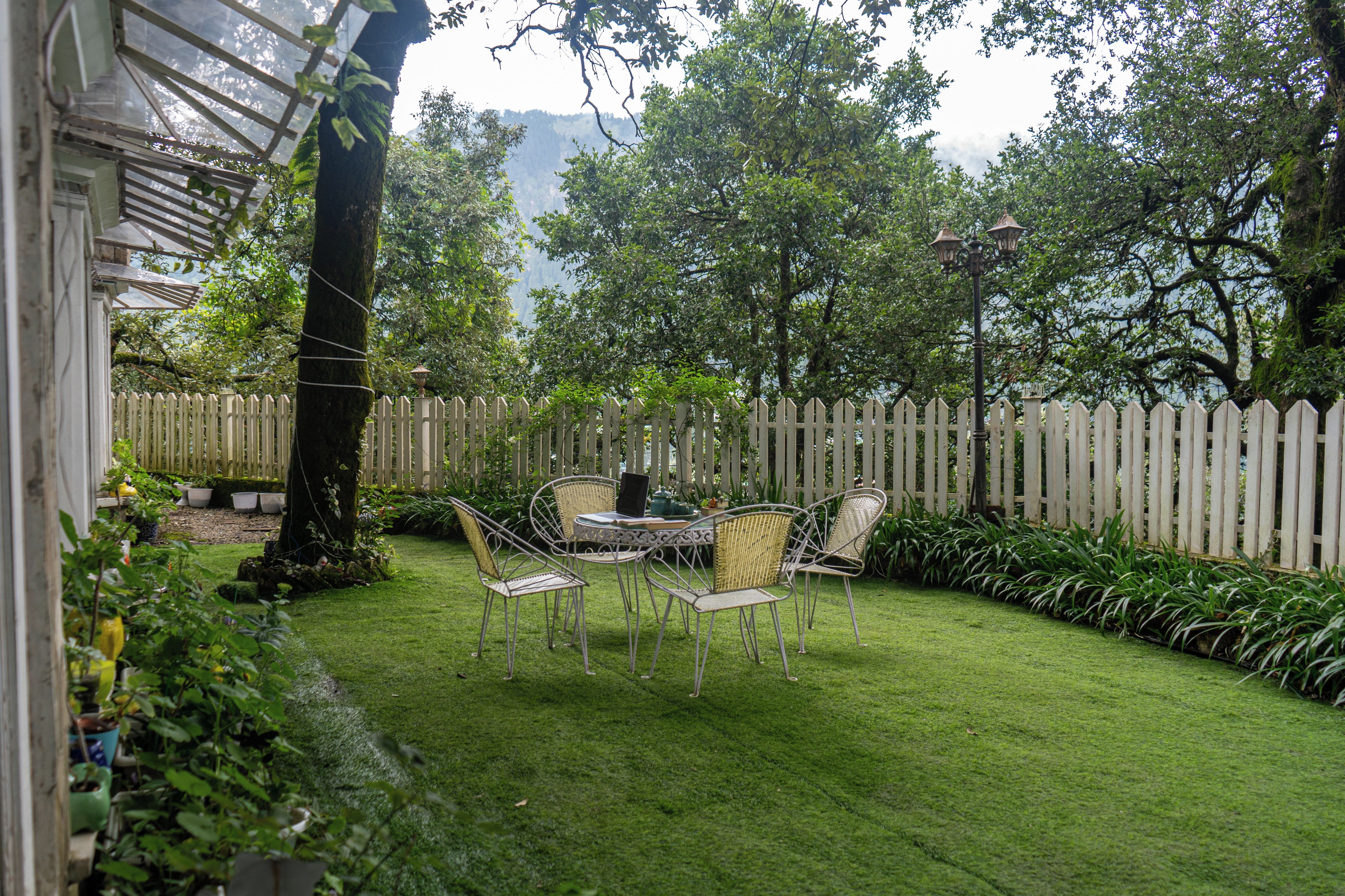 A patio with a table and chairs, surrounded by a wooden fence and lush greenery.