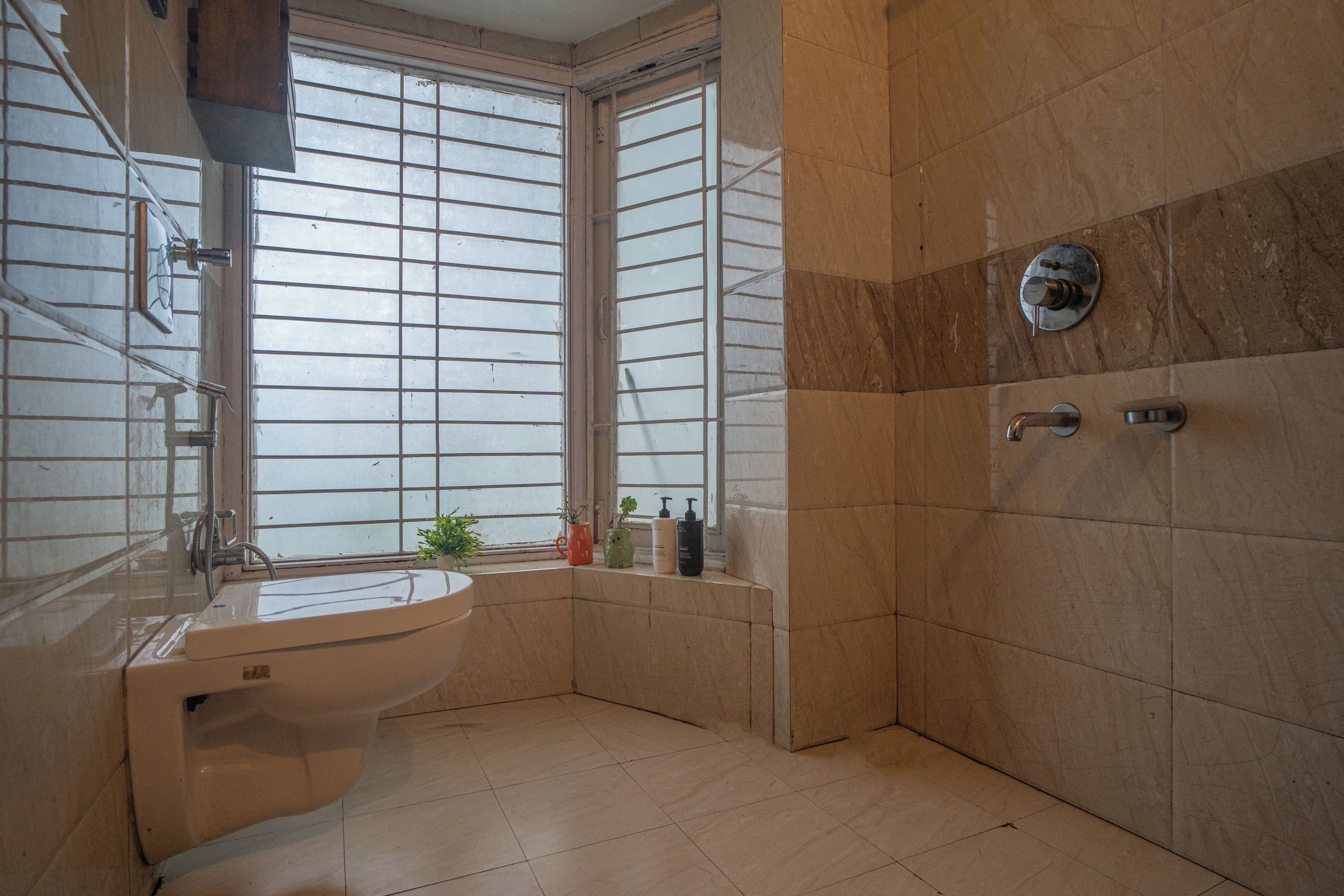 A bathroom with a sink, a shower, and a window with blinds.