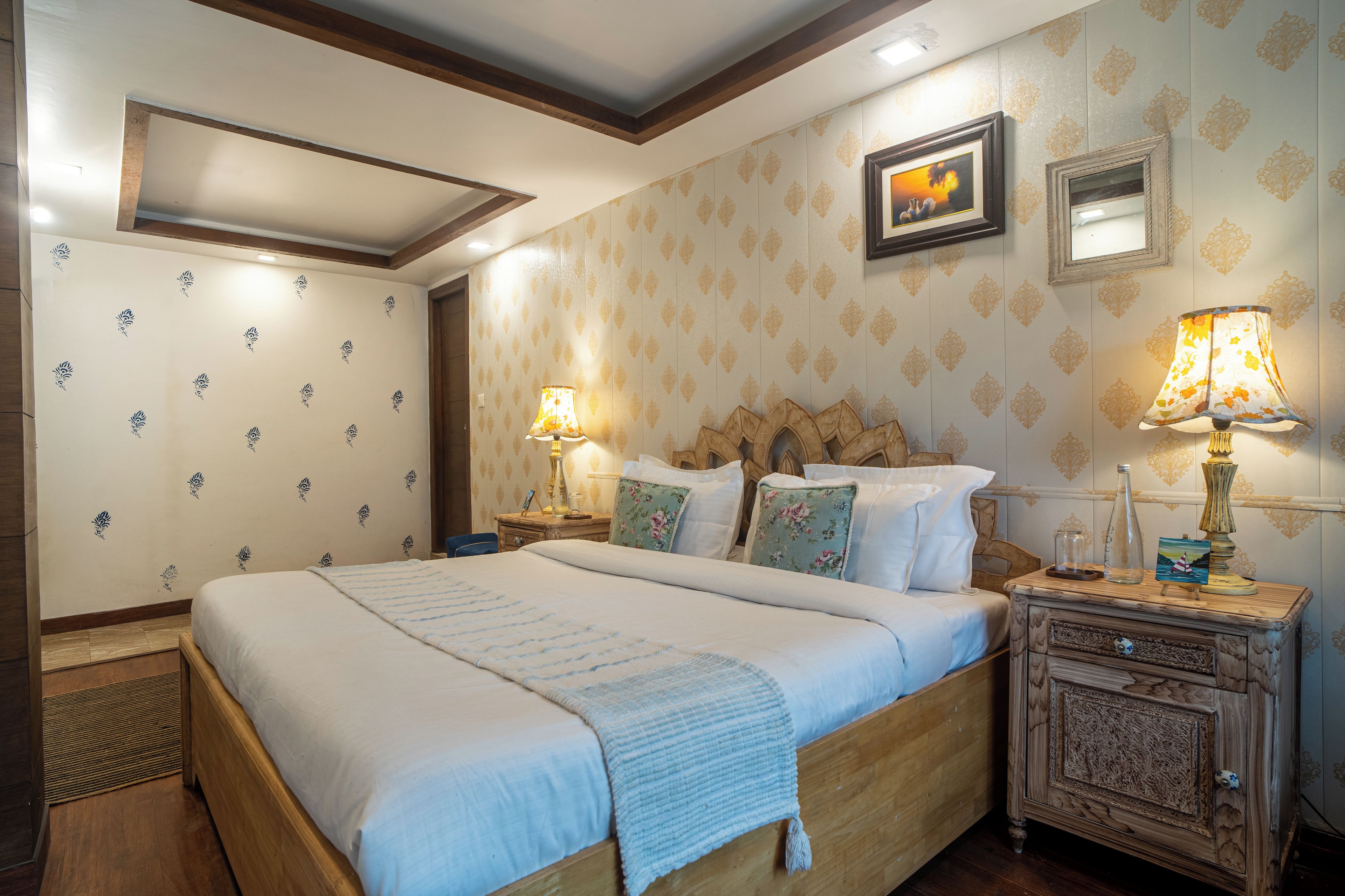 A bedroom with a large bed, wooden headboard, floral-patterned wallpaper, and two bedside lamps.