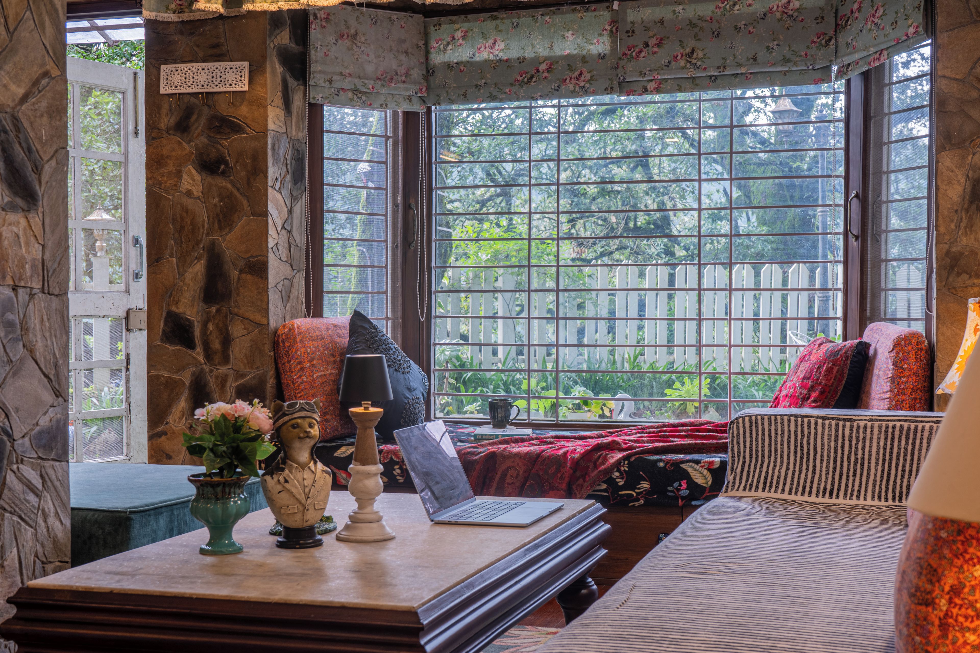 Una habitación acogedora con pared de piedra, un ventanal con vistas a la vegetación, una mesa con una computadora portátil y un globo decorativo.