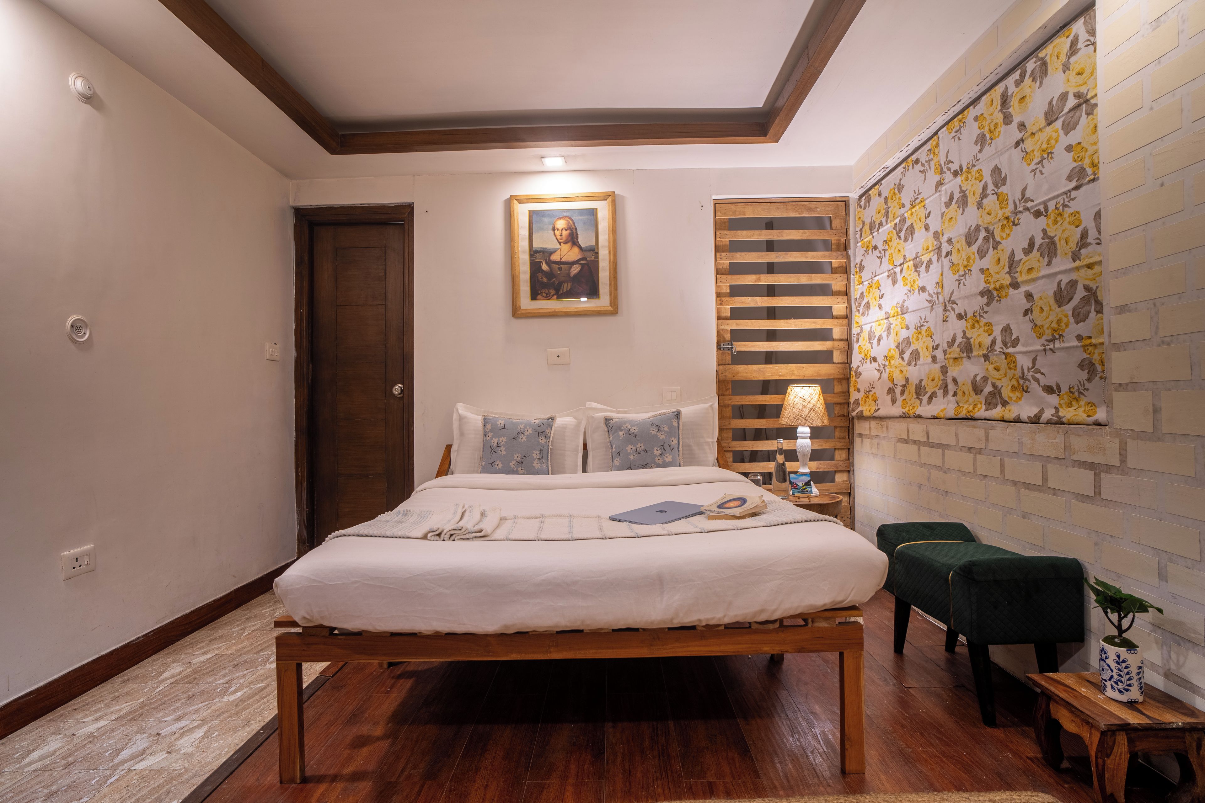 A bedroom with a wooden bed, a nightstand, a lamp, a small table with a plant, and a wall with floral wallpaper.