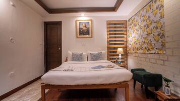 A bedroom with a wooden bed, a nightstand, a lamp, a small table with a plant, and a wall with floral wallpaper.
