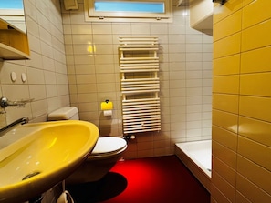 Une salle de bain avec un lavabo jaune, des toilettes blanches et un sol rouge.