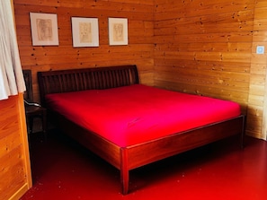 Ein Zimmer mit Holzwänden, einem Bett, einem Sessel und drei gerahmten Bildern an der Wand.
