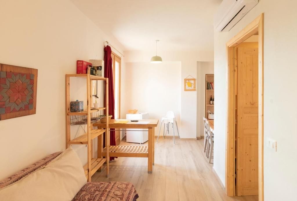 Ein Zimmer mit einer Couch, einem Holztisch, einem Stuhl, einem Bücherregal und einer Tür.